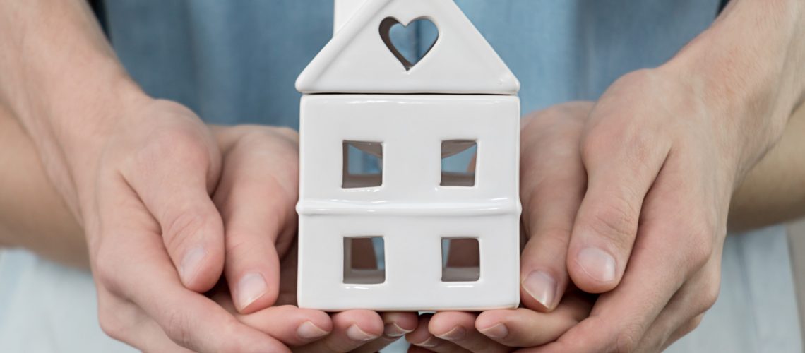 young-family-is-holding-toy-house-in-hands-cozy-man-people-home-finance-property-buy-sale-concept_t20_a8kKEx